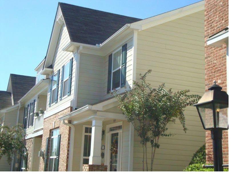 Two-storey home with repainted cream siding, white trim, brick base and dark shutters under a clear sky